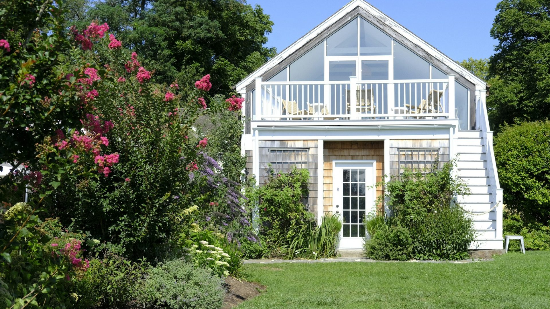 Small white house with a porch and wooden deck in a green yard (illustrative image)
