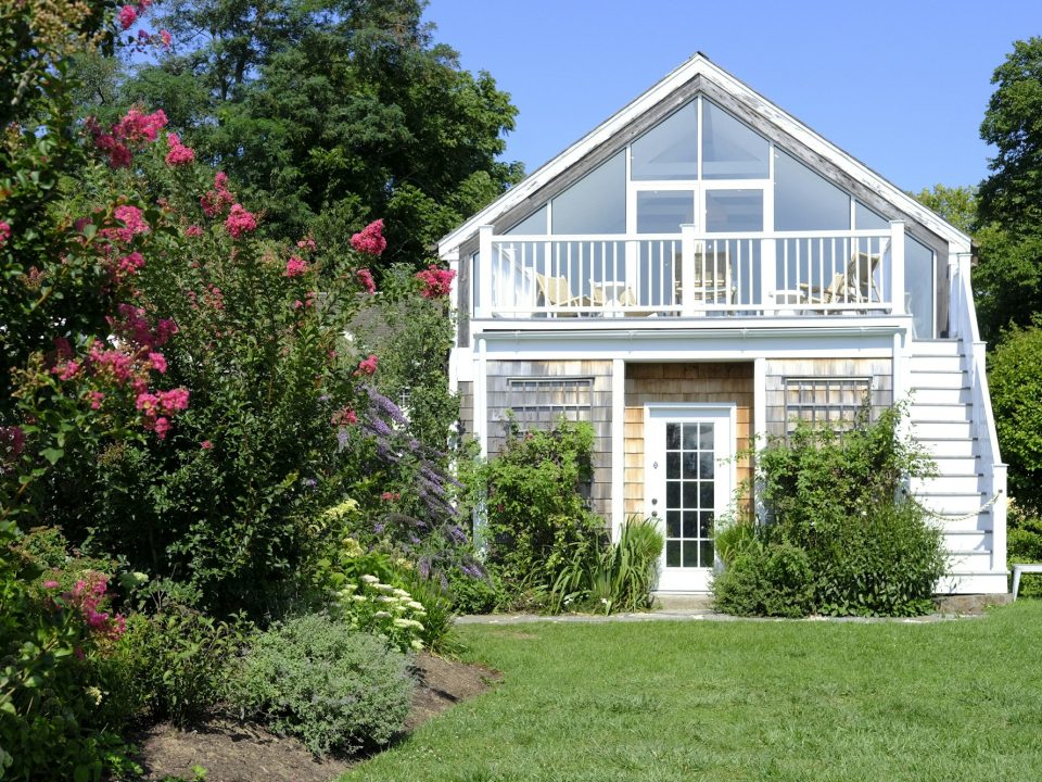 Small white house with a porch and wooden deck in a green yard (illustrative image)